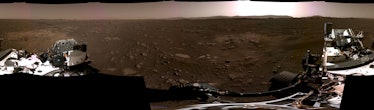 A panoramic view of Mars which includes some parts of the rover with the sun over the horizon