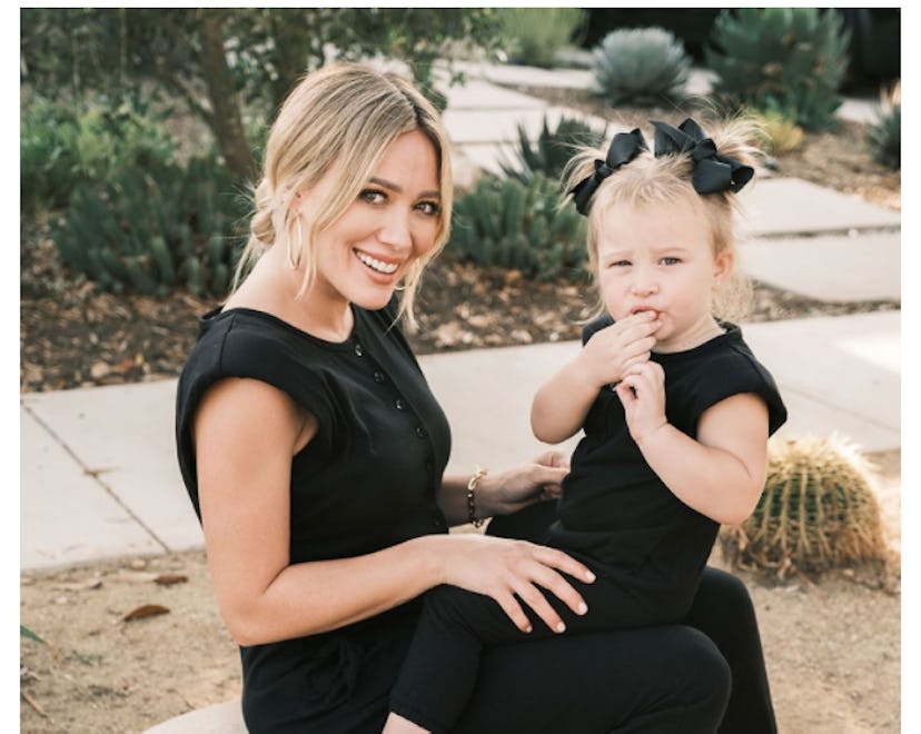 Hilary Duff in black short-sleeve and pants romper with little girl on her lap in matching romper