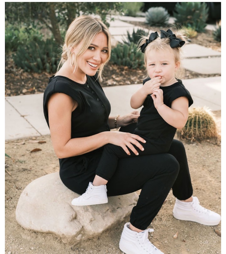 Hilary Duff in black short-sleeve and pants romper with little girl on her lap in matching romper