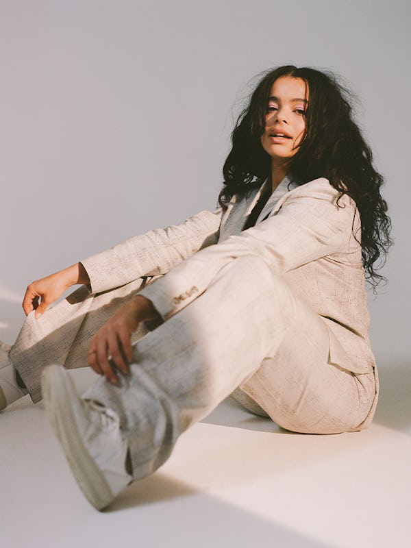 'It's A Sin' star Lydia West sitting on the ground in a studio wearing all-white suit and sneakers