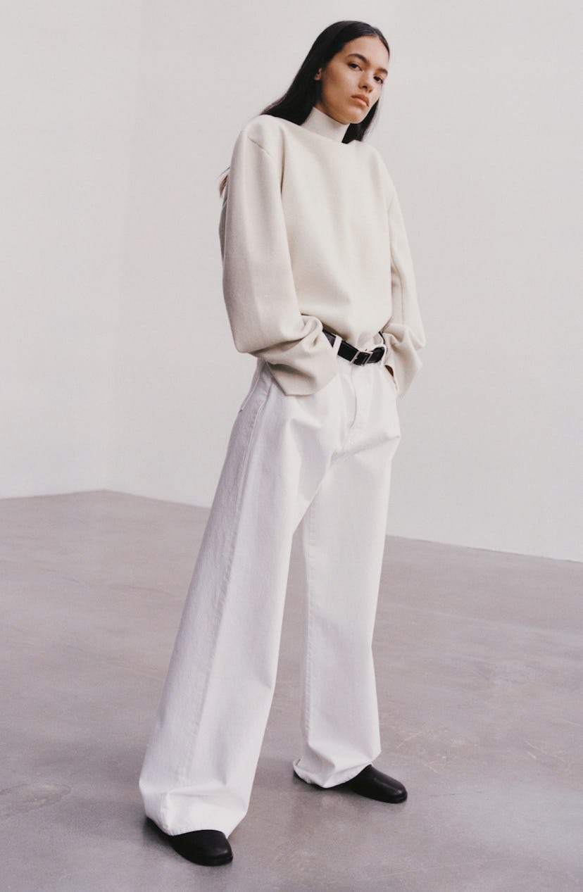 A model in a white turtleneck and white wide-leg pants with a black belt 