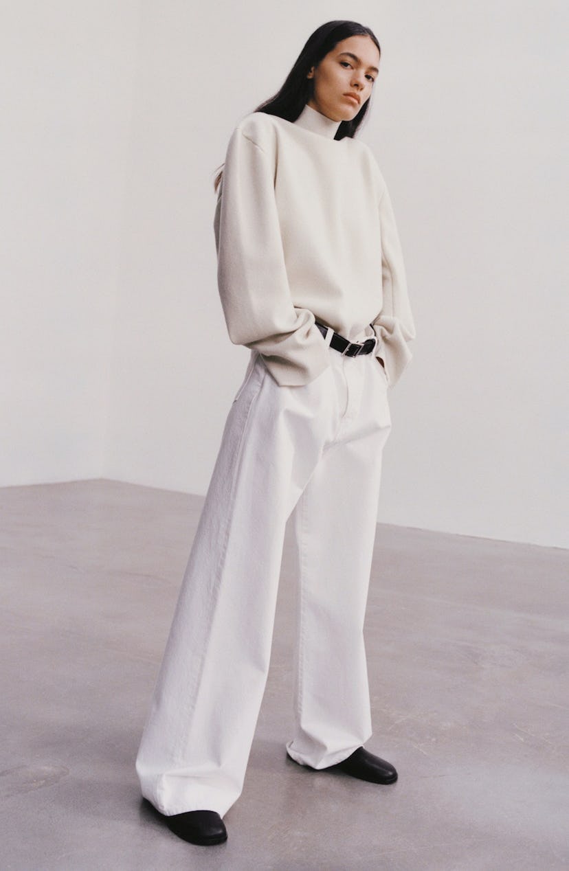 A model in a white turtleneck and white wide-leg pants with a black belt