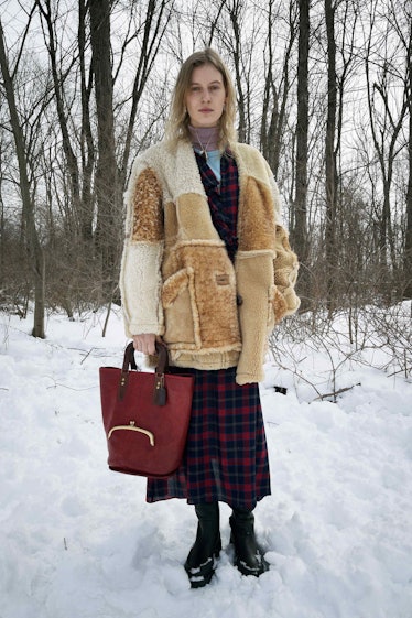 A model in a fur jacket and plaid skirt with a red bag by Coach