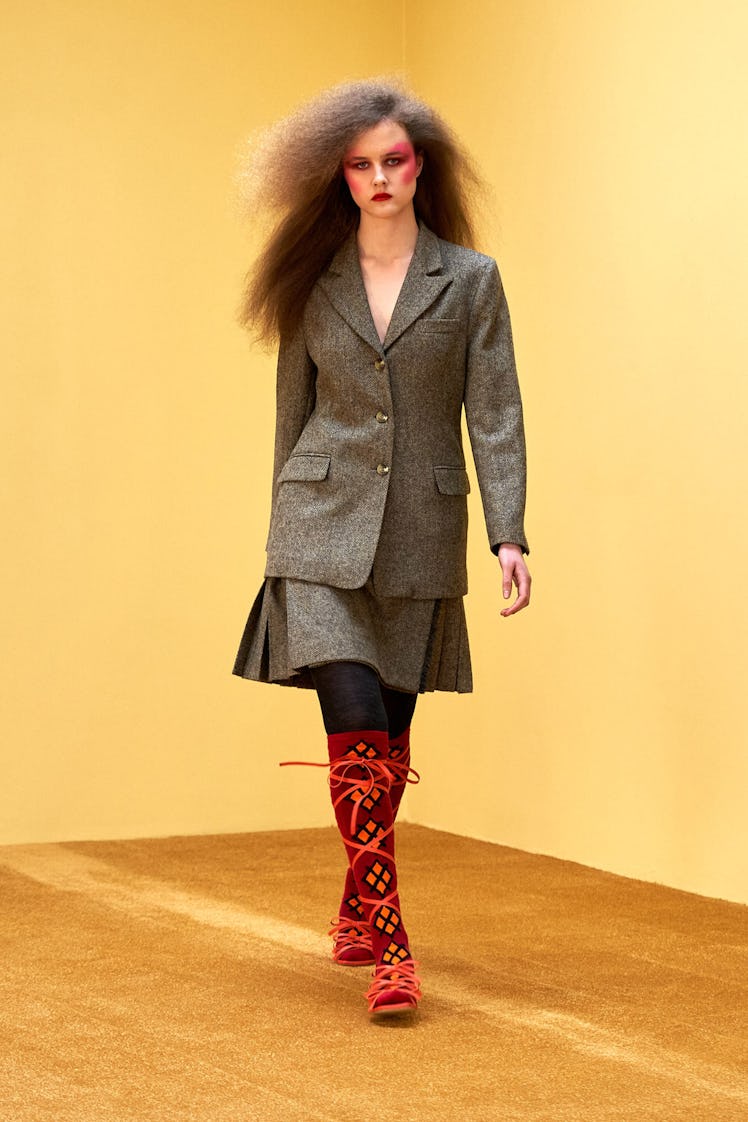 A model in a Molly Goddard grey blazer and skirt and orange socks and sandals at the London Fashion ...