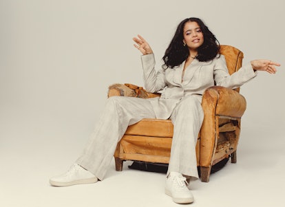 Lydia West posing full-profile in a chair wearing an all-white suit and sneakers