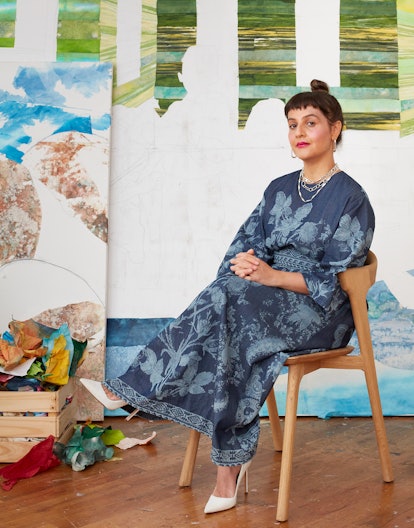Mari Berrio sitting on a chair in her Brooklyn studio in a long dark blue dress and white heels 