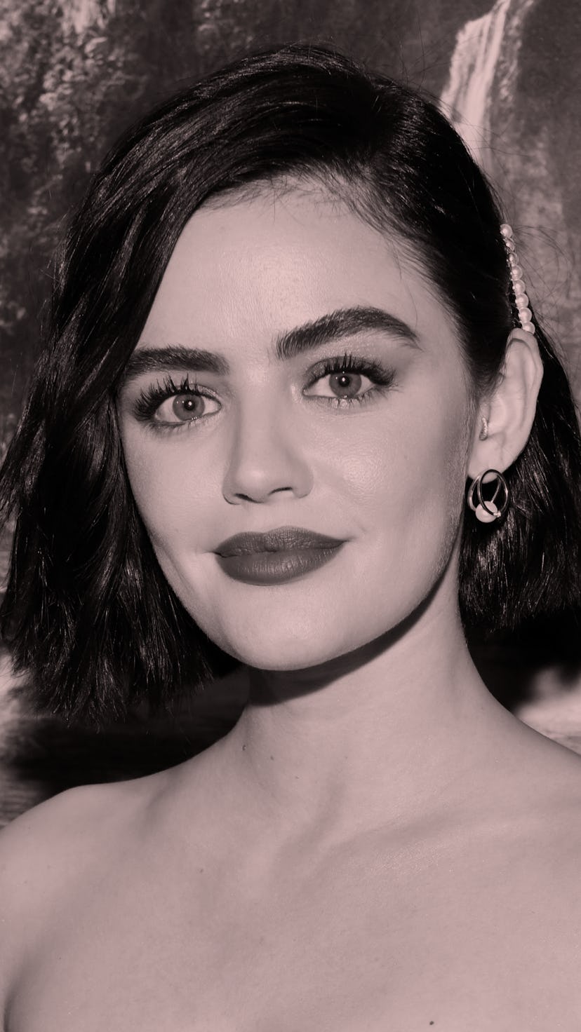 Lucy Hale, wearing pink lipstick, stands against backdrop of fake waterfall
