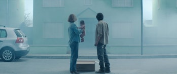 Imogen Poots, a baby, a cardboard box, and Jesse Eisenberg stand in front of a house.