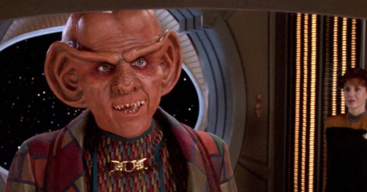 The Ferengi alien Quark, seen in colorful garb, with a Starfleet officer in the background