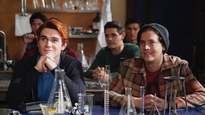 Archie and Jughead smile while sitting at a desk in science class in 'Riverdale.'