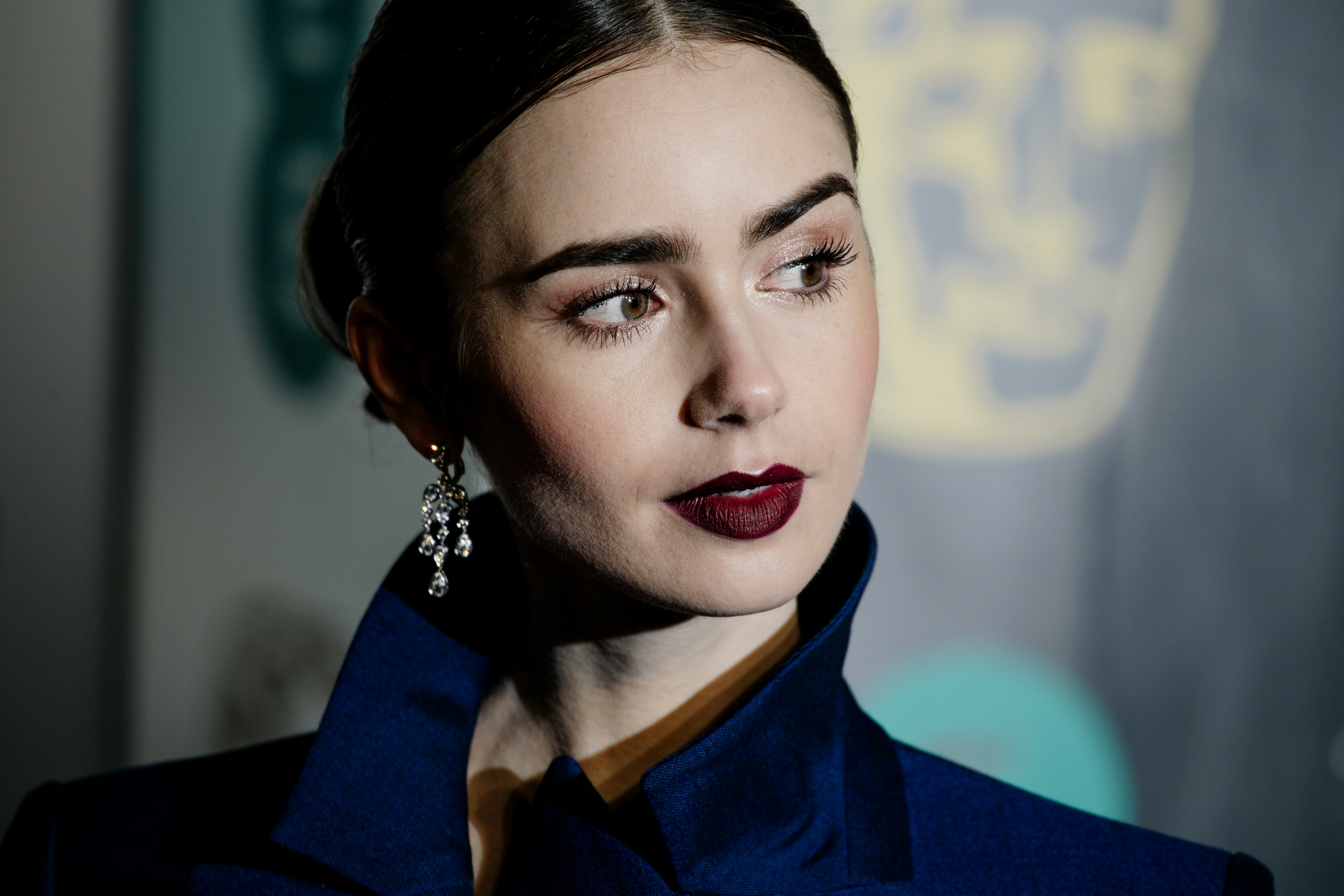 Lily Collins wears dark lipstick, along with a middle part, and her hair pulled back