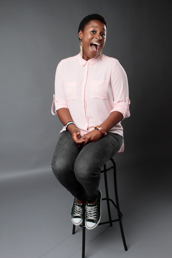 Issa Rae in a light pink button down shirt on a stool in a studio. 