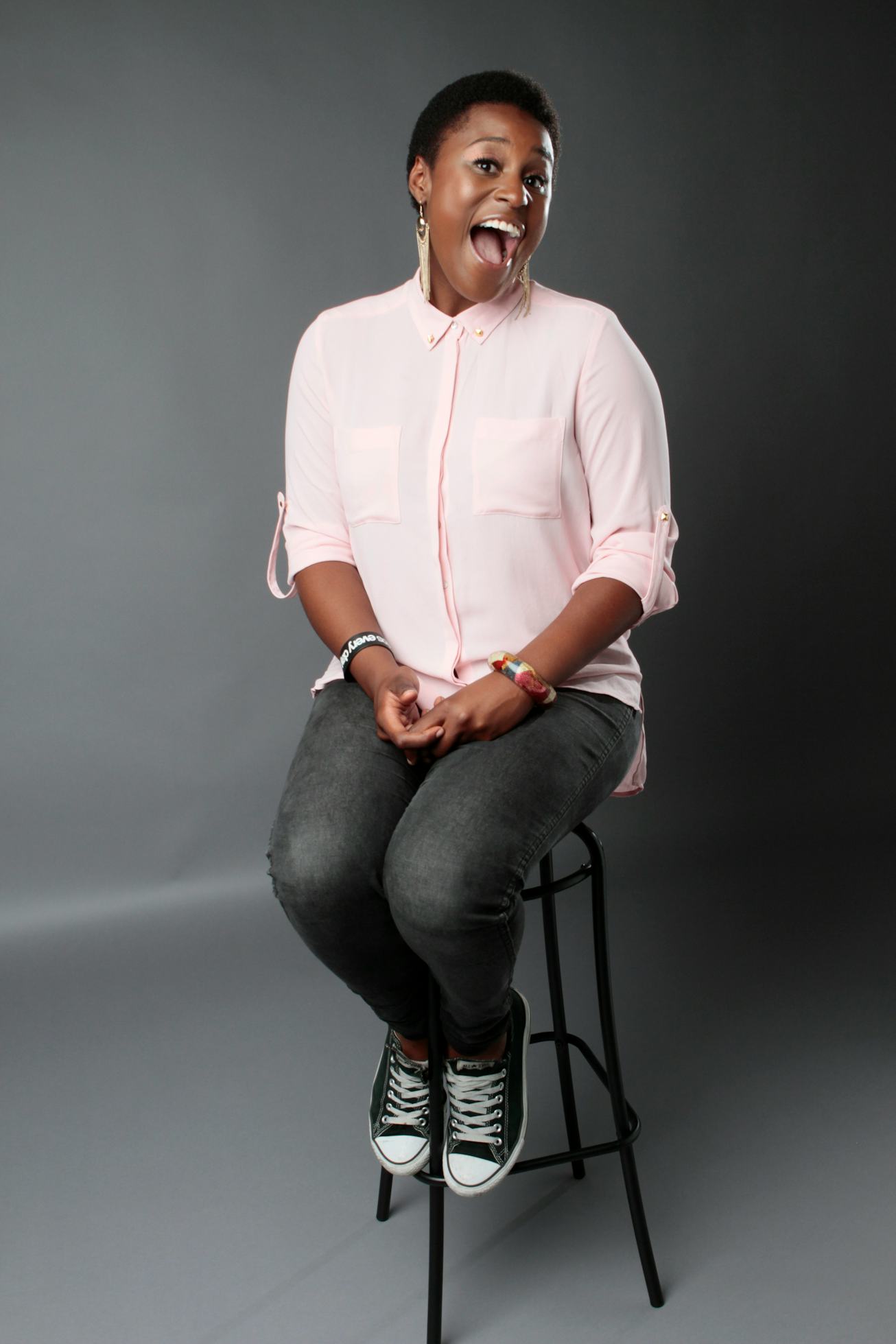 Issa Rae in a light pink button down shirt on a stool in a studio. 