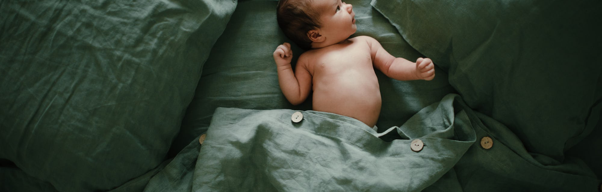 baby lying on bed with green sheets