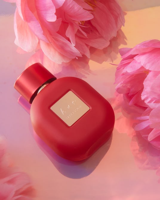 Red Hayley Kiyoko fragrance bottle near flowers.