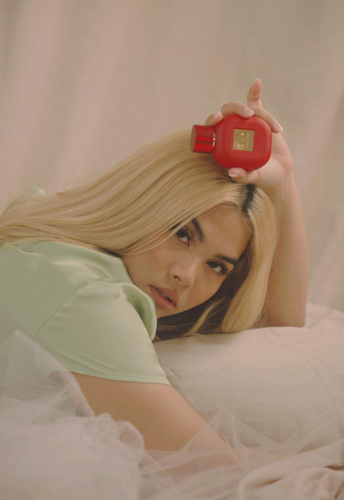 Artist Hayley Kiyoko in mint green blouse holding red bottle of perfume.