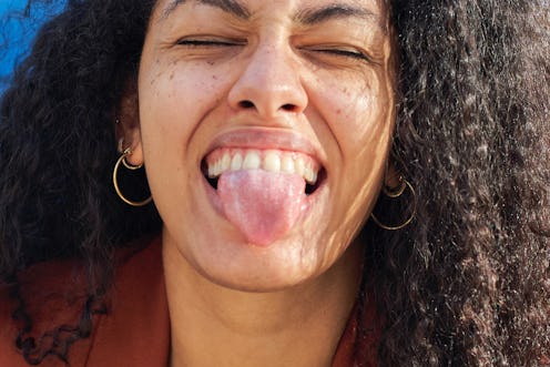 A woman sticks out her tongue close up. COVID tongue may be a sign of COVID.