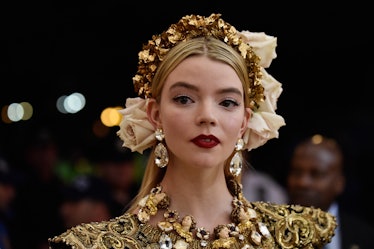 Taylor-Joy at the Met Gala wearing a gold ornate costume with her signature bold lip.