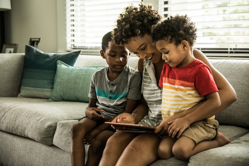 mother using tablet with young sons on couch 