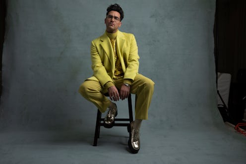 Dan Levy sitting in yellow pants, jacket, tie and shirt