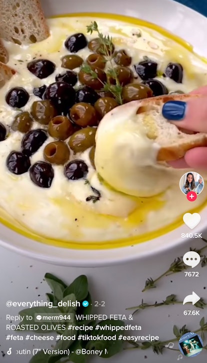 A woman dips some bread into a whipped feta and roasted olives dip. 