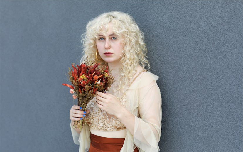 A portrait of Juliet Quick holding a bouquet of red flowers. She's standing against a gray wall.