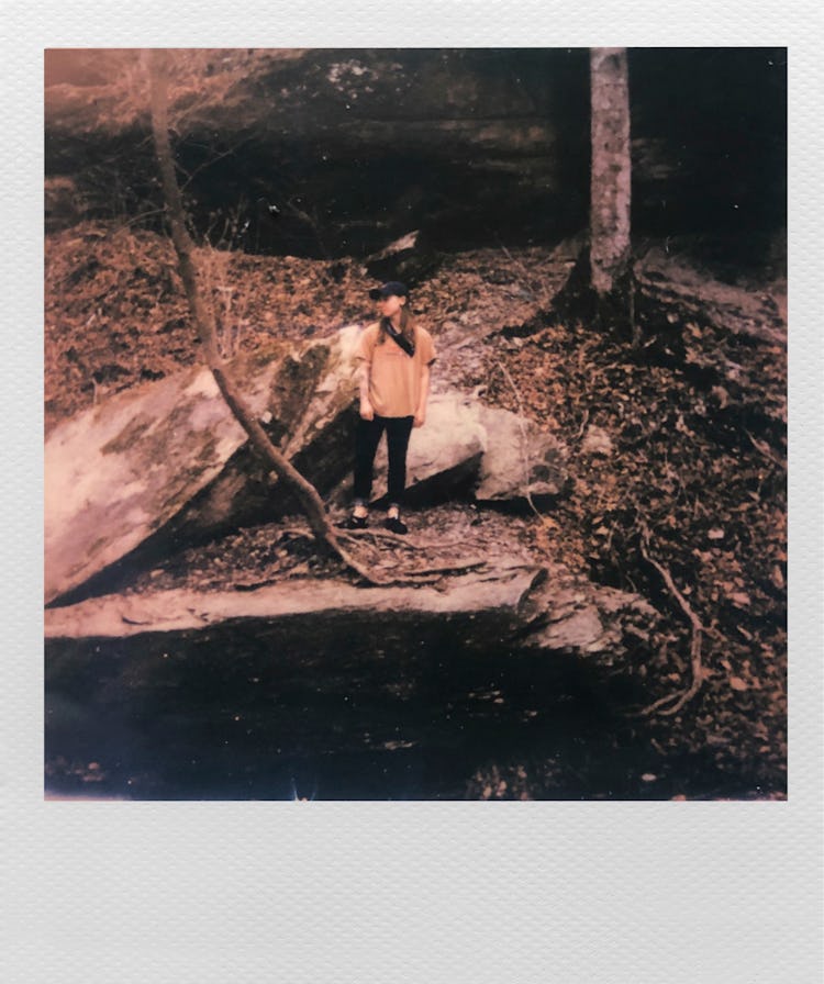 Polaroid of Julien Baker in the woods standing on a rock by a river