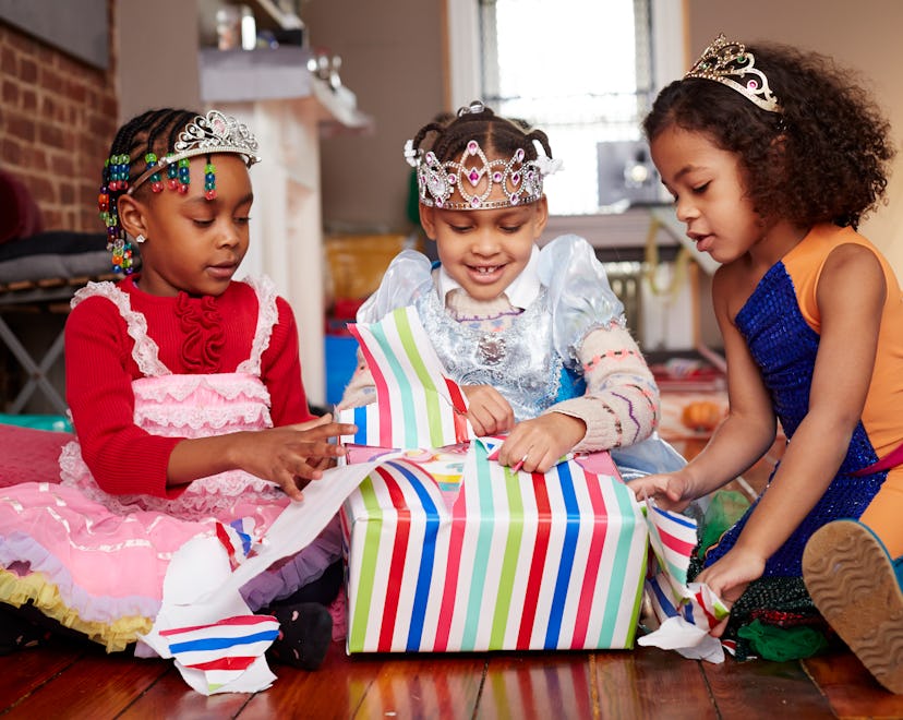 three girls wearing tiaras and opening presents 