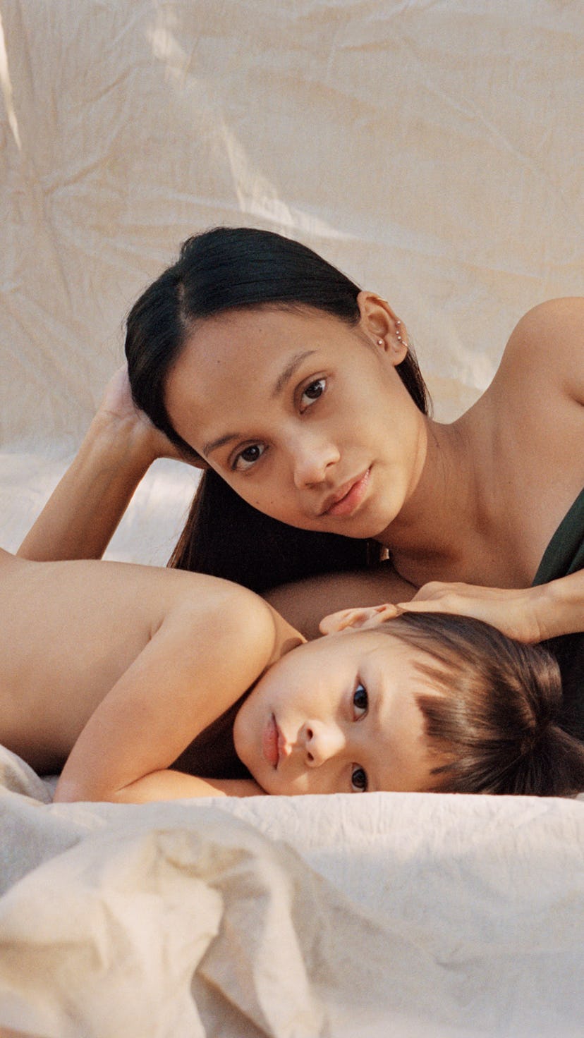 A pregnant woman lying on a bed next to her toddler both posing and looking at the camera
