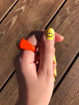 A closeup of a hand with yellow nail polish and a black smiley face