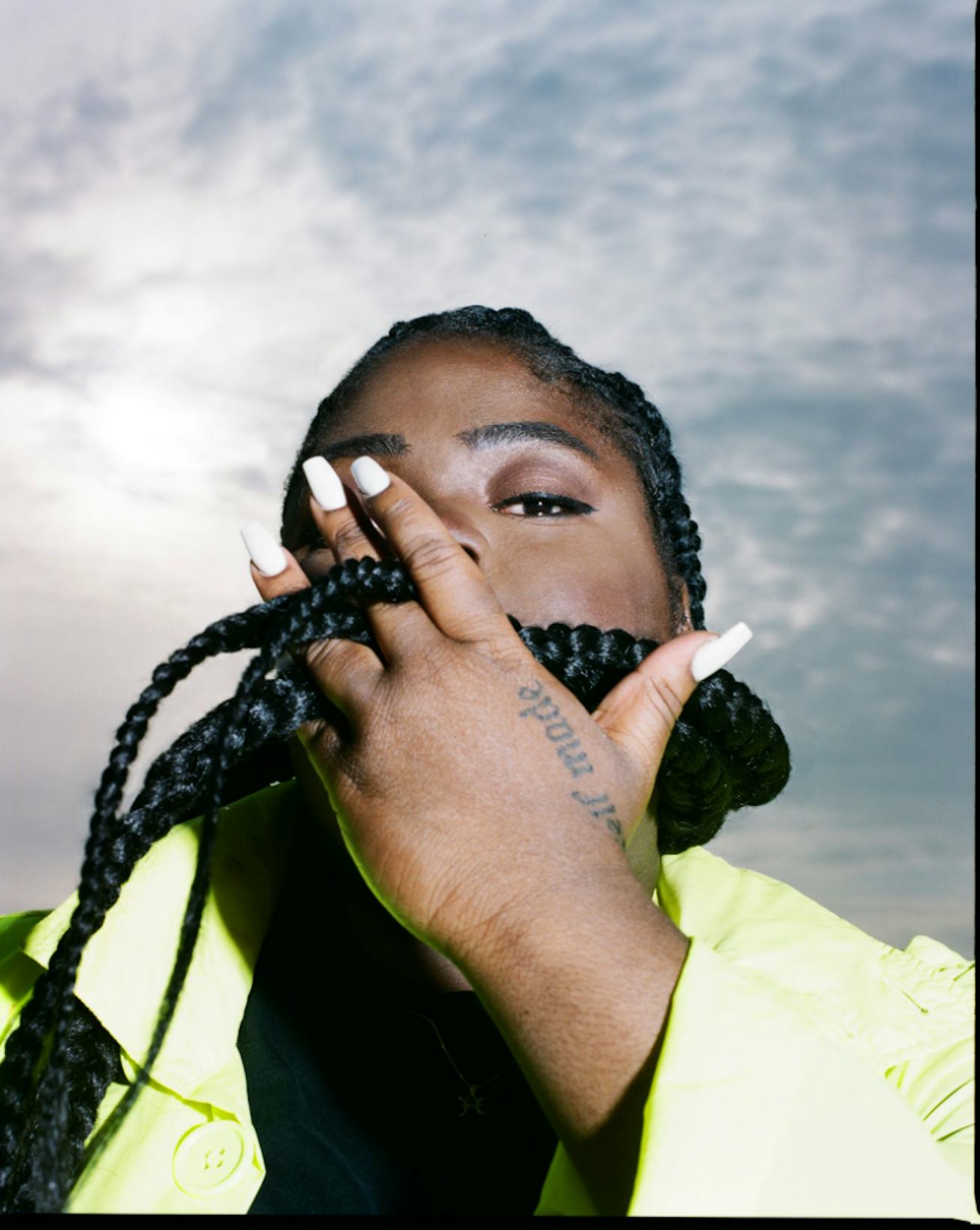 A portrait of CHIKA. She holds one of her braids in her hand in front of her face.