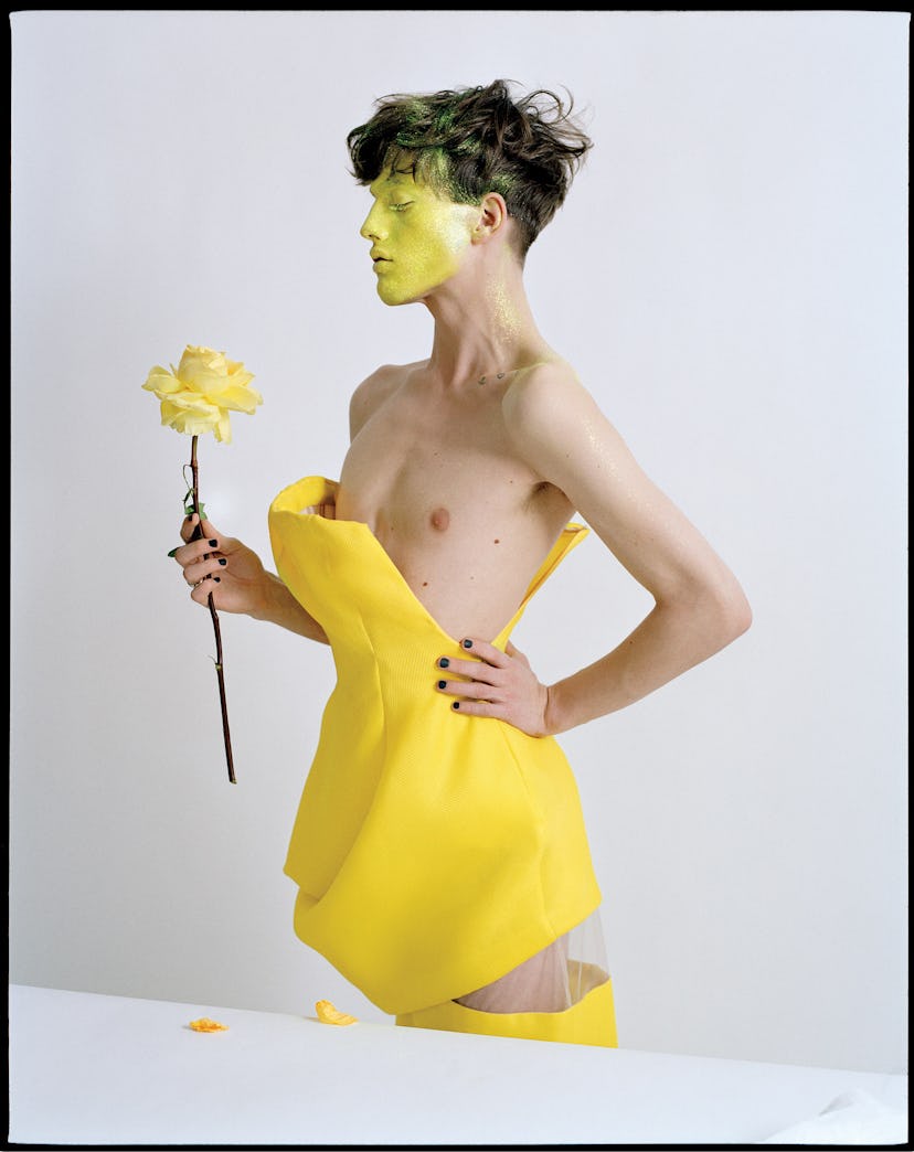 A man standing in a yellow dress and holding a yellow flower