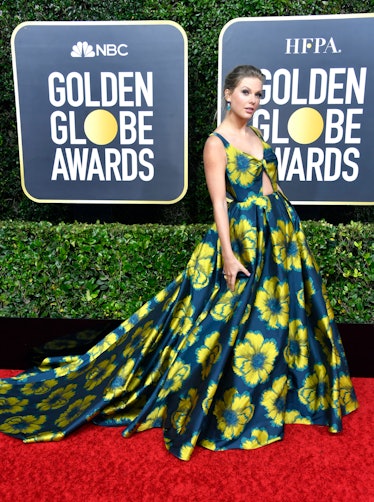 Taylor Swift at the Golden Globes in a dark blue gown with yellow flowers and her hair up 