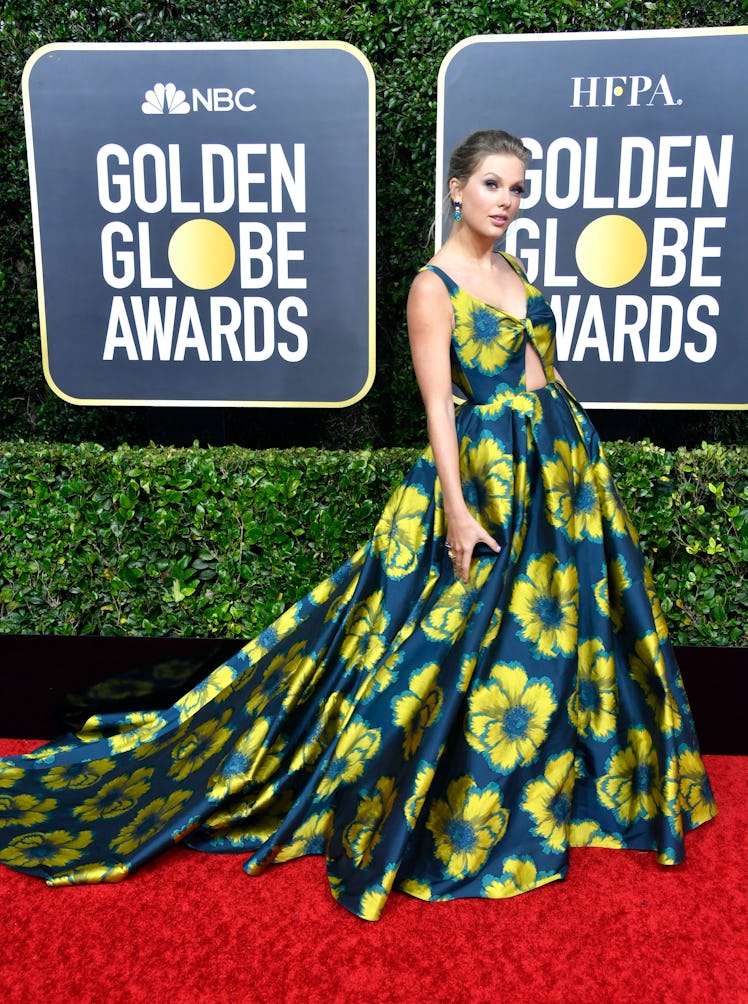 Taylor Swift at the Golden Globes in a dark blue gown with yellow flowers and her hair up 