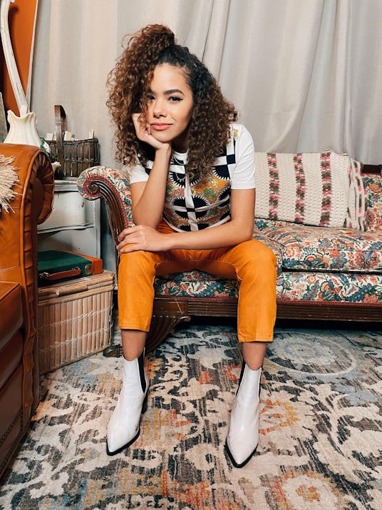 Antonia Gentry sitting in her living room in a checkered shirt, yellow leather pants and white platf...