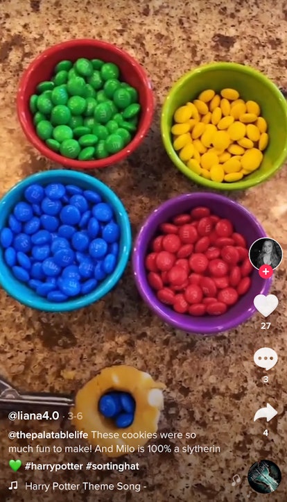 Four bowls of red, green, blue, and yellow M&M's sit on a kitchen counter with a woman holding a sco...