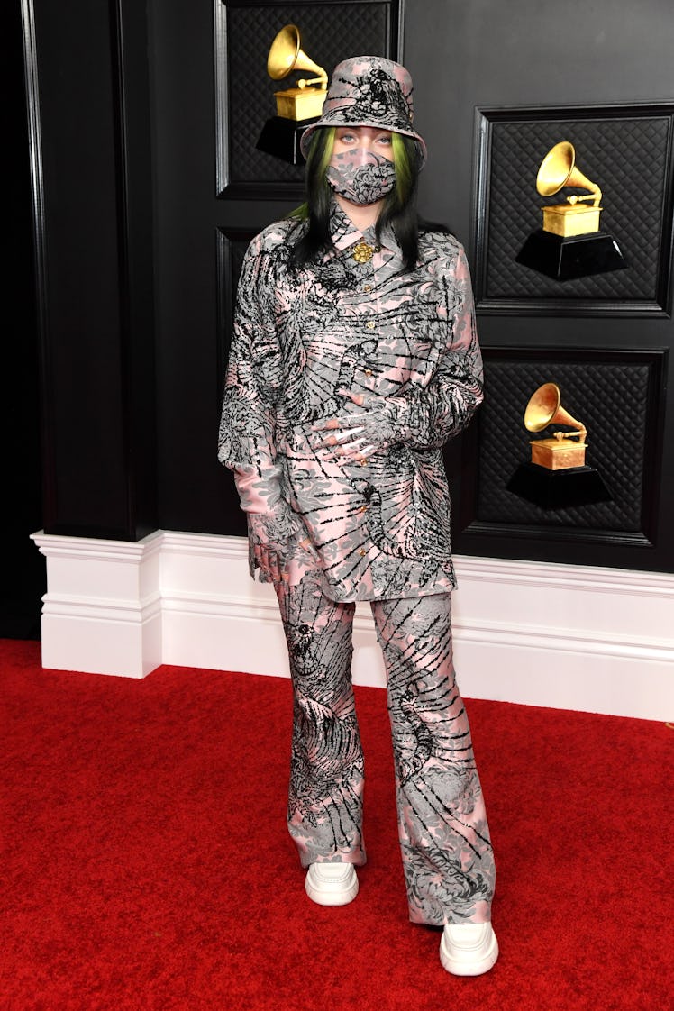 Billie Eilish on the red carpet wearing pink and gray-colored pants, a shirt, and a hat with black l...