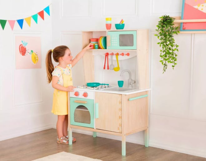B. Toys Wooden Play Kitchen, little girl playing with toy; best gifts for 3-year-olds