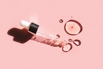 A pipette and droplets of face serum with bakuchiol on a pink background
