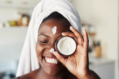  A woman with a towel on her head, smiling while holding a jar of face cream with bakuchiol
