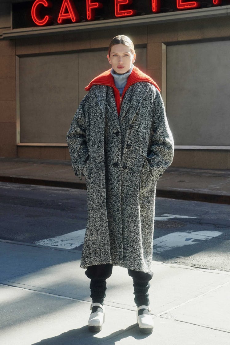 A model in a grey overcoat and red sweater by Tory Burch