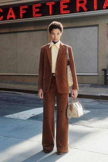 A model in a brown suit with a yellow shirt and two bags by Tory Burch