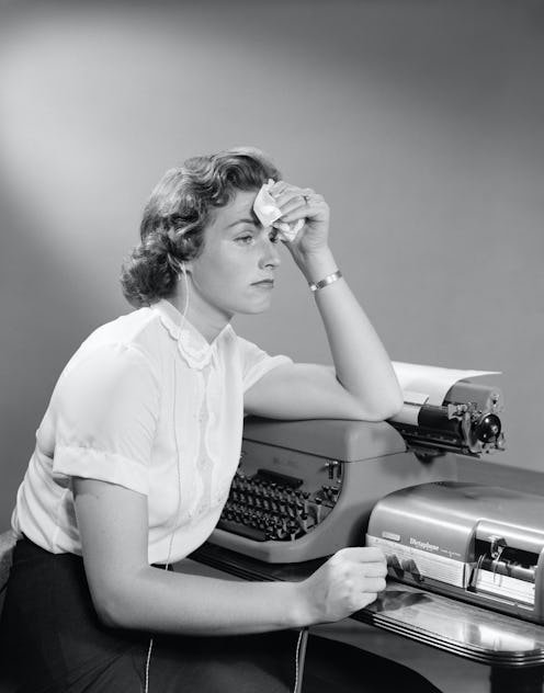 An anxious woman mops her forehead with a fever at her desk next to a typewriter. A mental health ex...