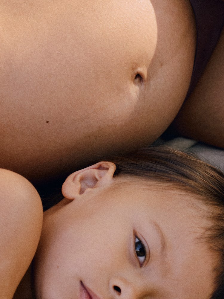 close-up of a pregnancy belly and a toddler snuggled next to it 