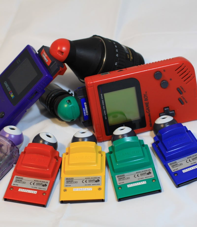 A family of different colored Game Boy Cameras with Game Boys and DIY camera lens attachments.