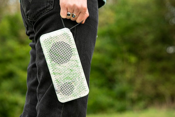 A view of a white and green Gomi speaker held next to a person's leg