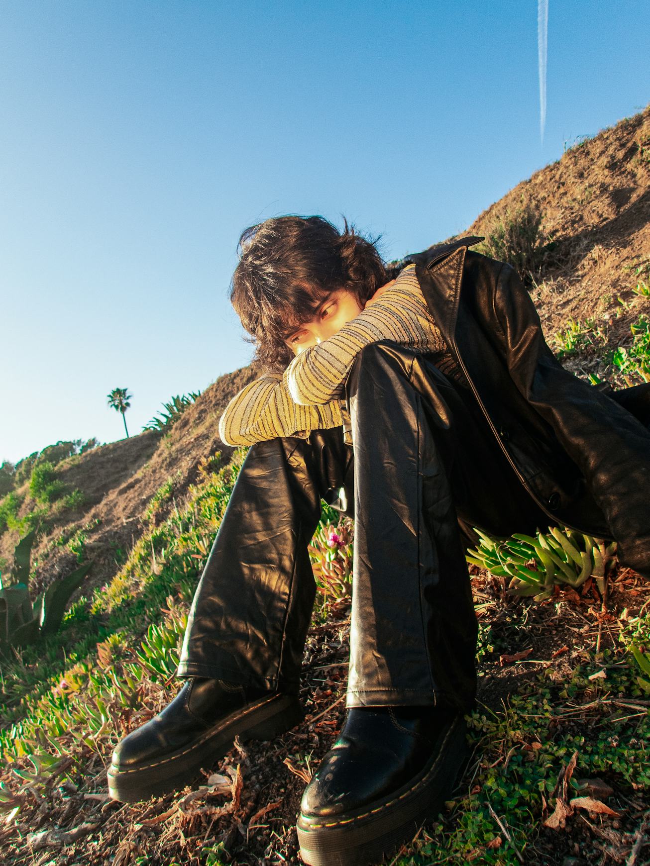 A portrait of musician KALI. She is sitting outside on the grass with her arms resting on her knees.