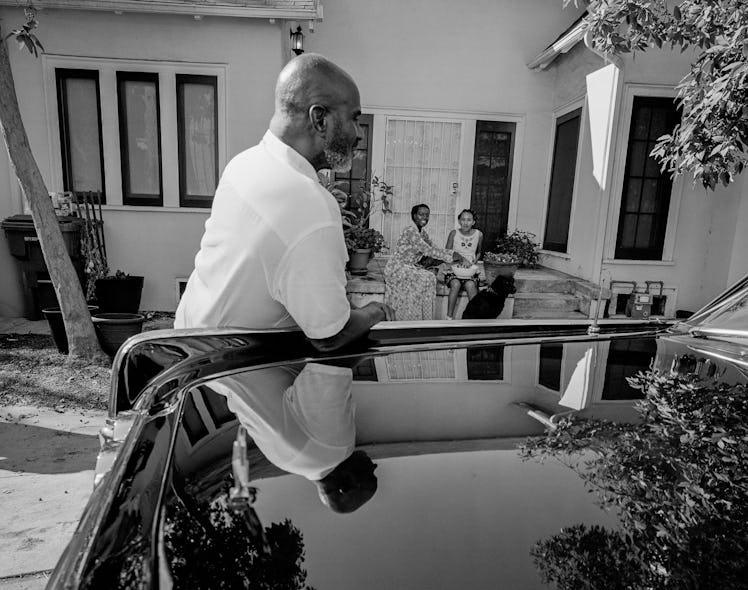 Julius Tennon in focus leaned against a car, with Viola Davis and Genesis Tennon in the background s...