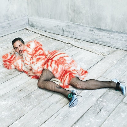 Marc Jacobs lying on the floor, wearing a furry red and white coat, fishnets, and blue heels