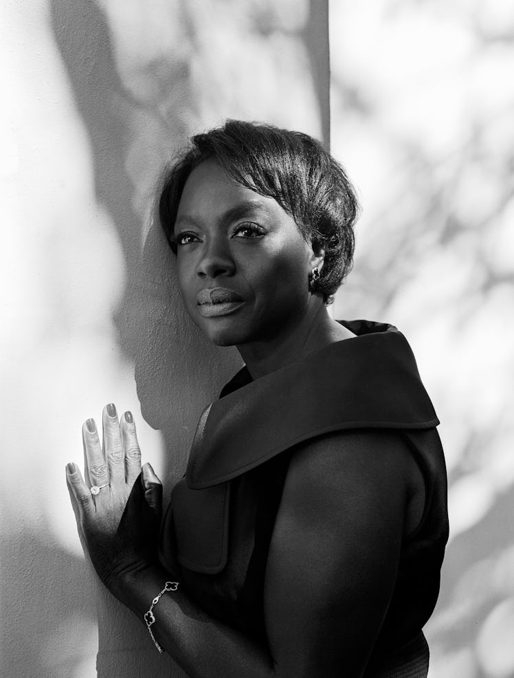 Viola Davis leaning against a wall in a black dress, Van Cleef & Arpels earrings & bracelet, and her...